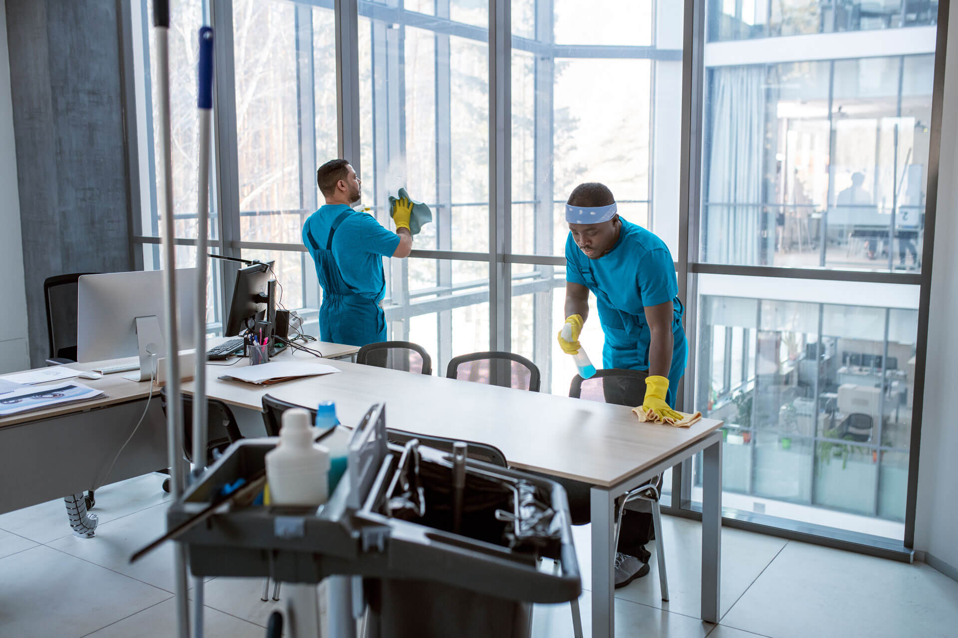 Two men providing cleaning service to a desk in an office.