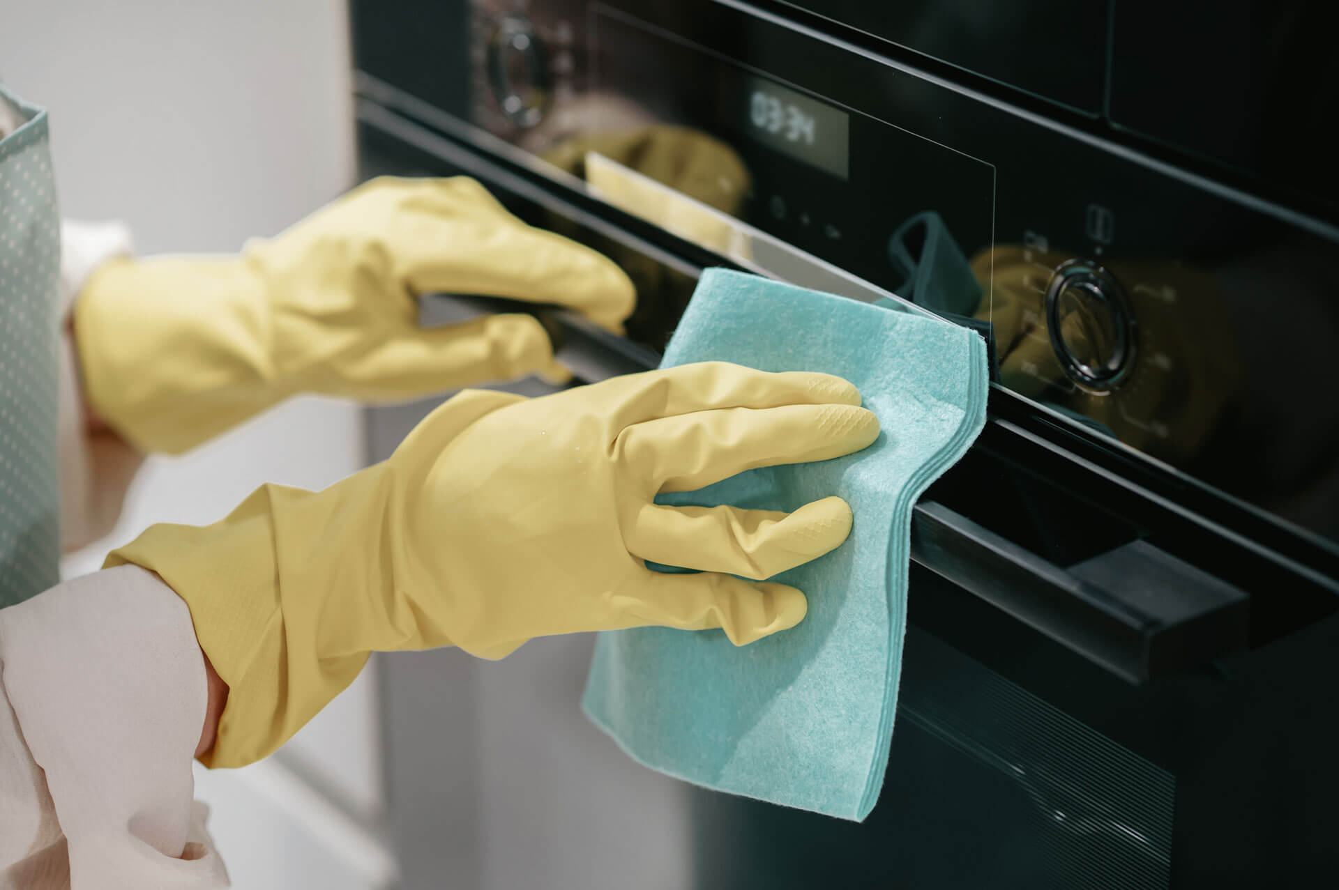A maid from Pompano Beach, Florida providing cleaning services while wearing yellow gloves and cleaning an oven.