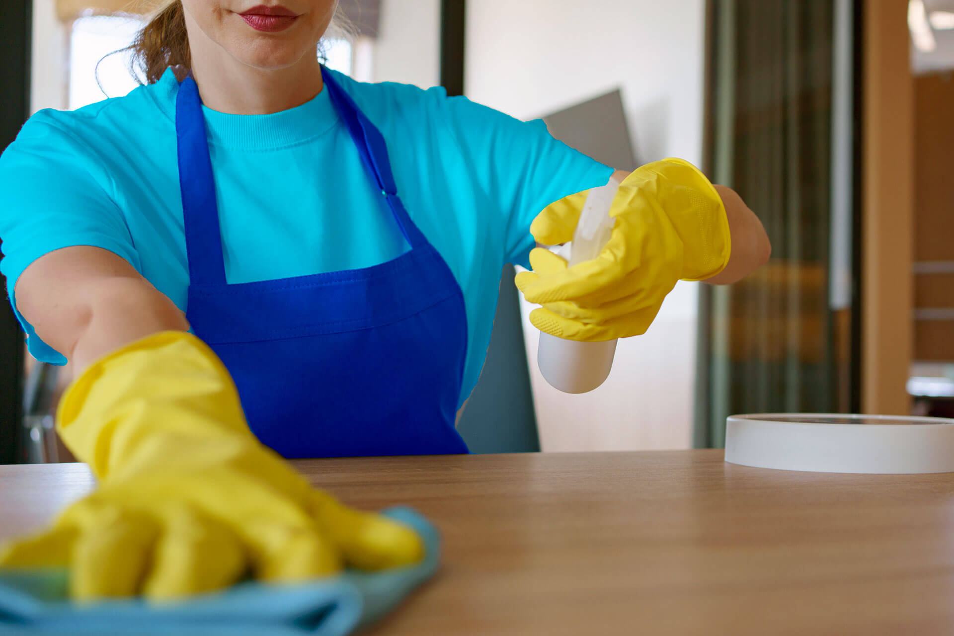 A maid from Laredo, Texas, wearing a blue apron and yellow gloves, cleaning a table for a cleaning service.